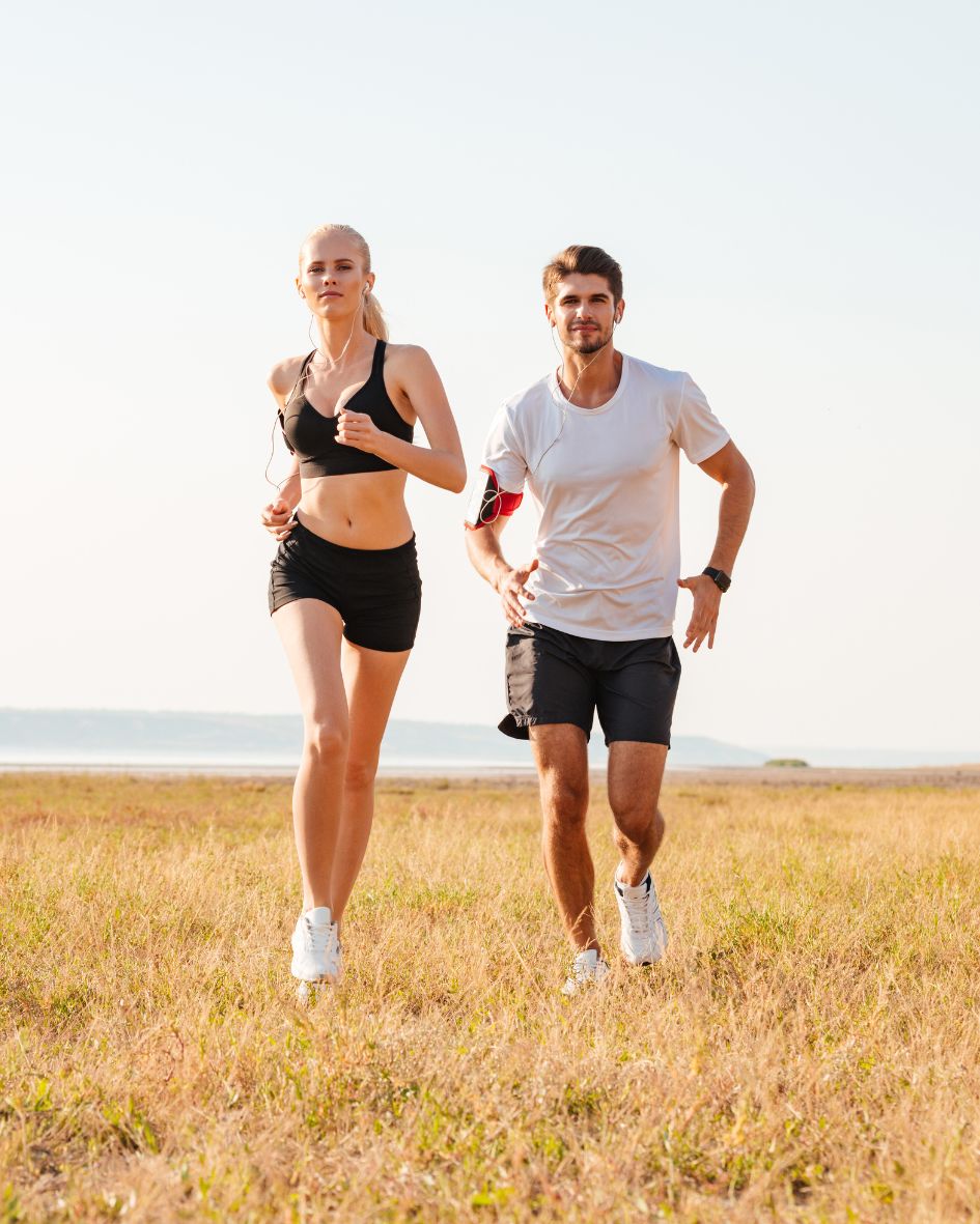 Two people running together in a field with a clear sky.